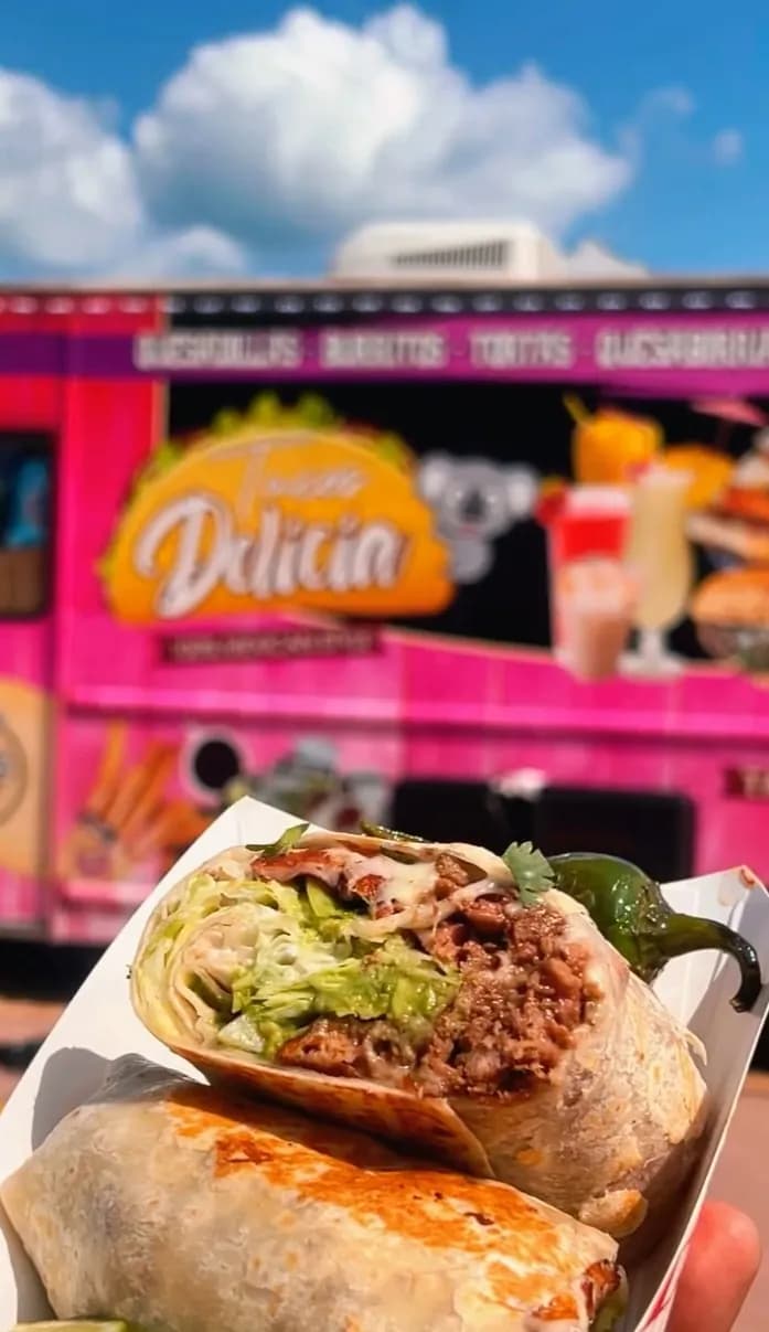 Loaded burrito held up in front of the Delicias Tacos pink food truck in Chicago