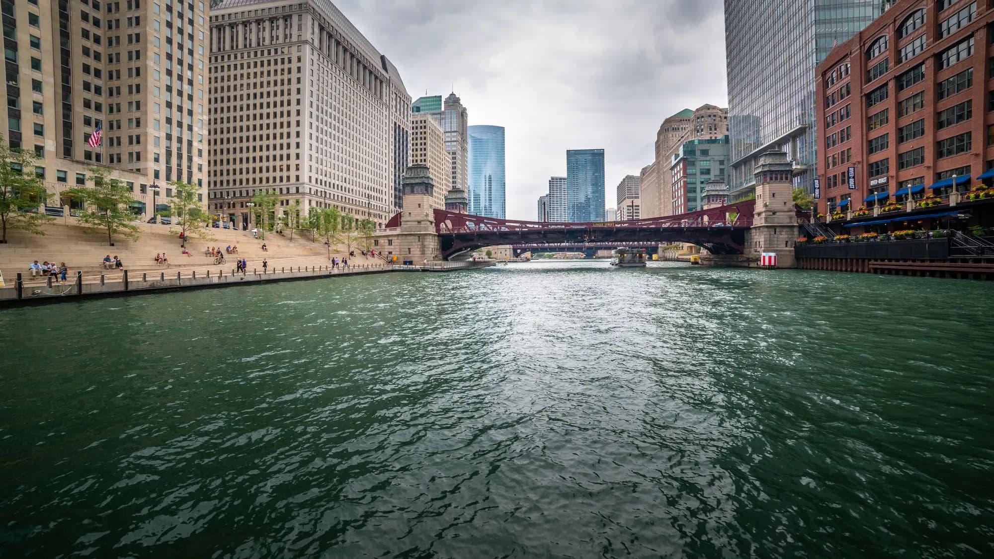 The Chicago River between downtown towers, with a red bridge and the riverwalk