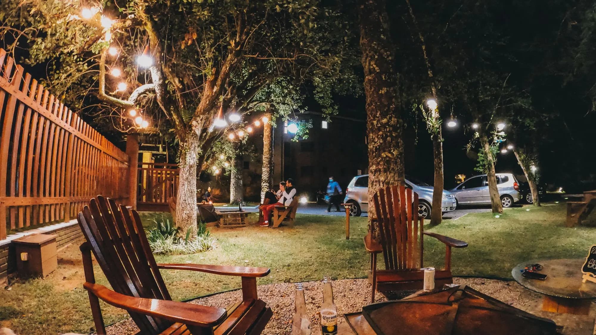 Backyard at night with string lights in the trees, deck chairs and a fire pit