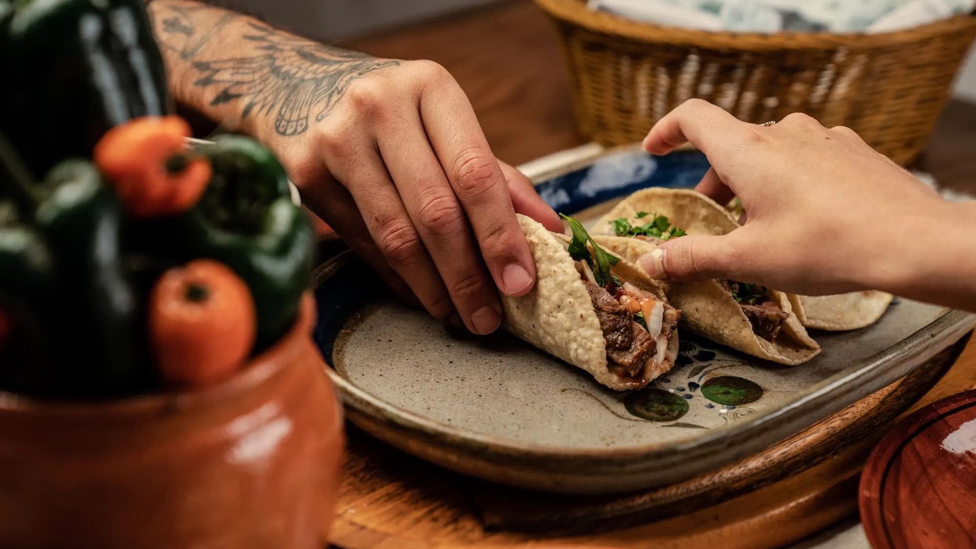 Two people reaching for Mexican street tacos on a plate at a shared table