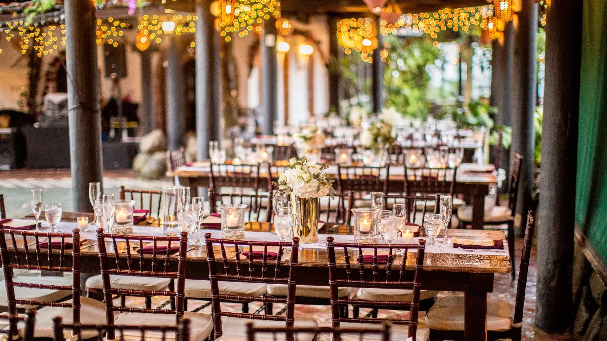 Long banquet tables laid with candles under warm string lights at an event venue