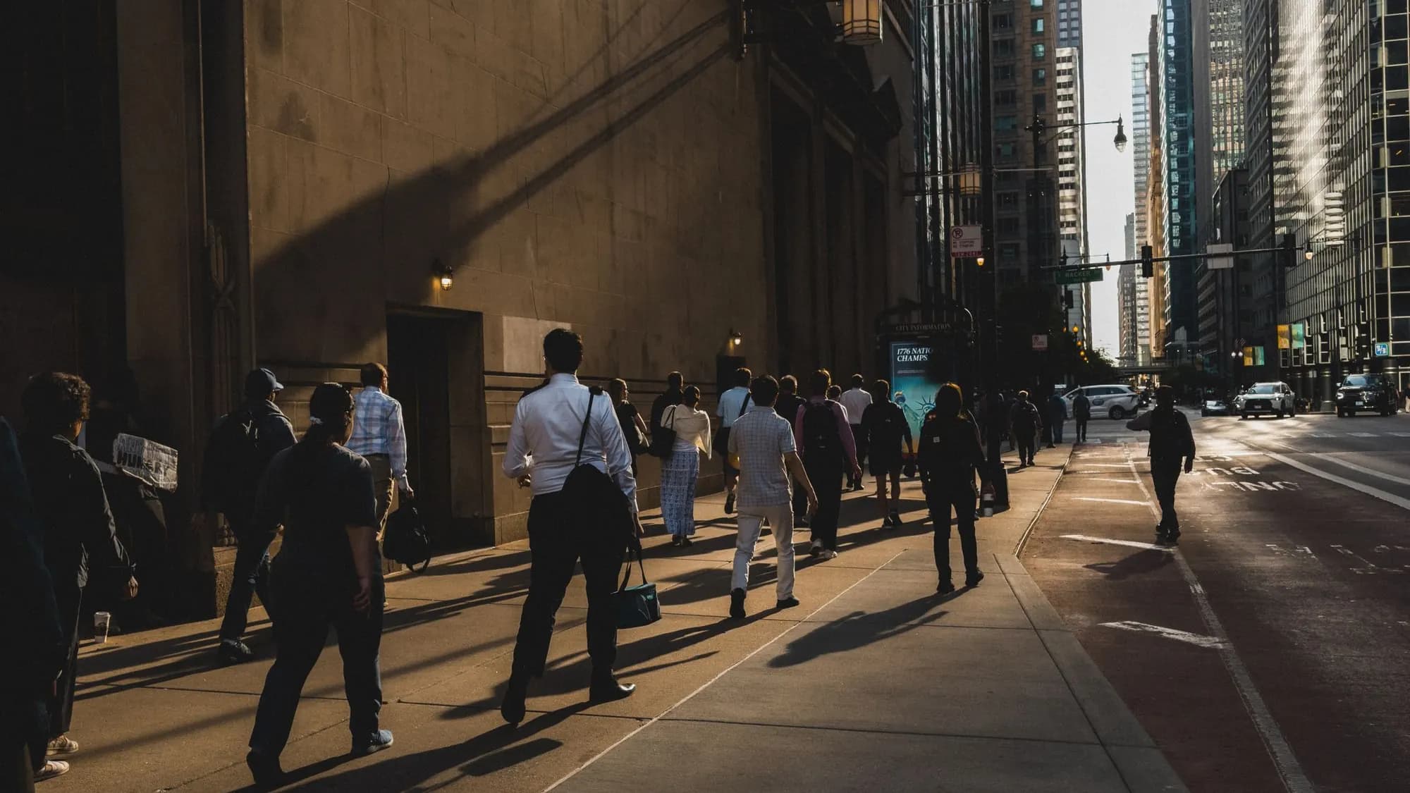 Office workers walking a sunlit sidewalk between towers in downtown Chicago