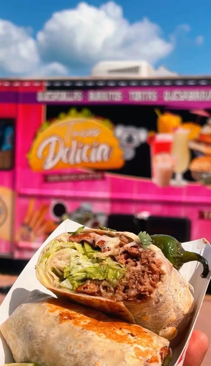 Loaded burrito held up in front of the Delicias Tacos pink food truck in Chicago