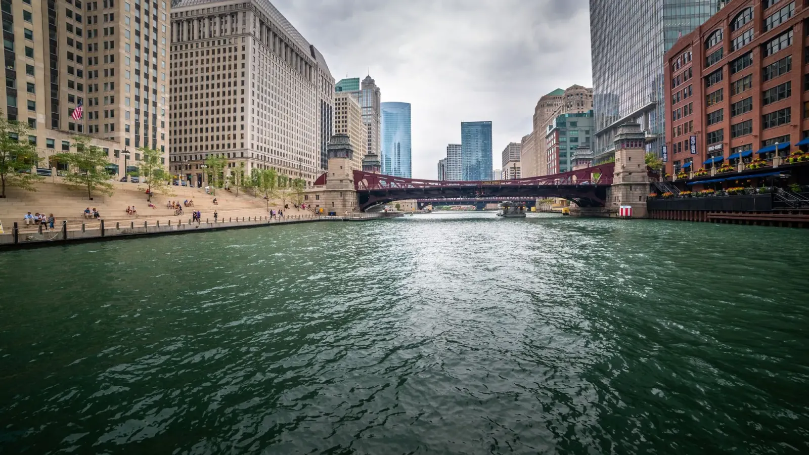 The Chicago River between downtown towers, with a red bridge and the riverwalk
