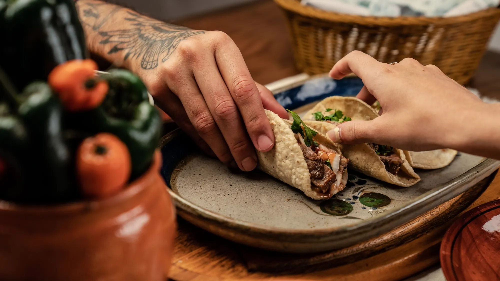 Two people reaching for Mexican street tacos on a plate at a shared table